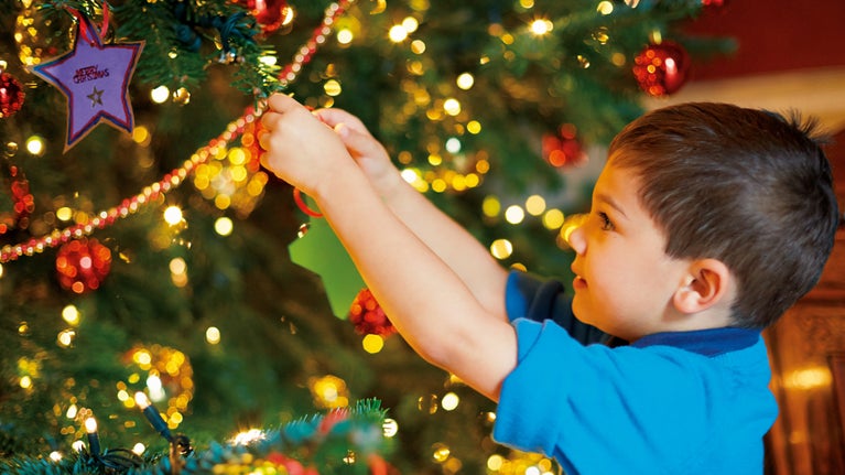 Images shows a young boy adding a star decoration to a Christmas tree at Attingham Park